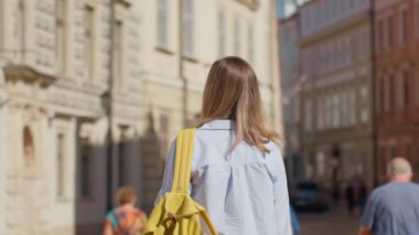 Polonya, Krakow 'da sarı sırt çantası taşıyan bir kadın yürüyor. Yaz günü Avrupa sokaklarını keşfeden kadın turist