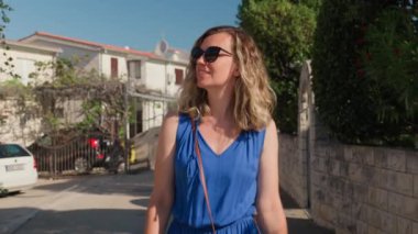 Hırvatistan 'ın kıyı kenti sokaklarında gezinen turistler, yaz tatilinde güneşli havanın keyfini çıkarıyorlar. Güneş gözlüğü takan ve mavi elbiseli güzel bir kadın dışarı çıkıyor.