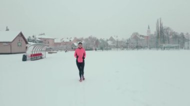 Stadyumda karla kaplı pistte koşan bir kadın. Karlı yolda koşan bir bayan sporcu. Kış sporları eğitimi kavramı