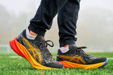 Close-up athlete wearing colorful Asics Novablast on artificial grass. Sportsman legs in sport sneakers on green grass. Wroclaw, Poland - November 6, 2024 clipart