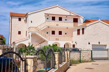 Dış merdiveni, balkonları ve çitli bahçesi olan bir ev. Hırvat mimarisi kıyı kasabasında. Yaz tatilleri için kiralık ev