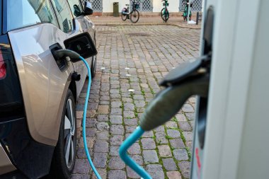 Şehir caddesinde halka açık bir istasyonda elektrikli araç şarj oluyor. Kablolu şarj pili takılı bir EV arabası. Sürdürülebilir ve çevre dostu ulaşım