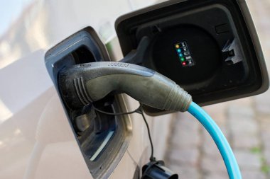 Şehir caddesinde halka açık bir istasyonda elektrikli araç şarj oluyor. Kablolu şarj pili takılı bir EV arabası. Sürdürülebilir ve çevre dostu ulaşım