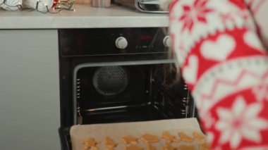 Kırmızı şenlikli kazaklı kadın Noel kurabiyelerini fırına koyuyor. Kış tatili için geleneksel zencefilli kurabiye pişirme süreci