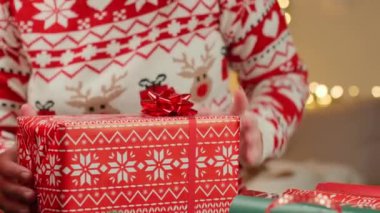 Noel süveteri giyen bir kadın Noel hediyesini ambalaj kağıdı ve kurdele masasıyla sarmış. Kış tatili için hediyeler hazırlanıyor.