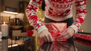 Noel hediyelerini kırmızı ve yeşil kağıda saran kadın elleri. Şenlikli kazaklı kadın kış tatili için hediyeler hazırlıyor. Noel ve Yeni Yıl Aile Gelenekleri