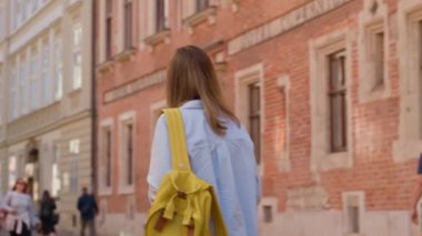 Polonya, Krakow 'da sarı sırt çantası taşıyan bir kadın yürüyor. Yaz günü Avrupa sokaklarını keşfeden kadın turist