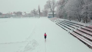 Stadyumda karla kaplı pistte koşan bir kadın. Karlı yolda koşan bir bayan sporcu. Kış sporları eğitimi kavramı