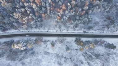 Karlı yolda giden beyaz arabanın hava manzarası kış ormanlarını kaplamıştı.
