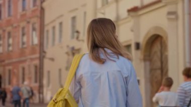 Polonya, Krakow 'da sarı sırt çantası taşıyan bir kadın yürüyor. Yaz günü Avrupa sokaklarını keşfeden kadın turist