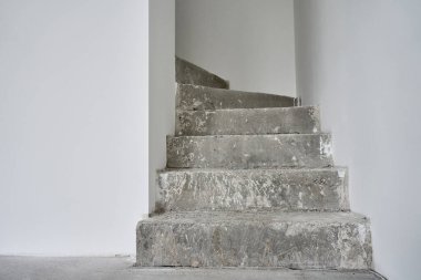 Tamamlanmamış beton merdivenleri ve tadilattan geçen beyaz duvarları olan boş bir daire. İnşaat halindeki binanın içi.