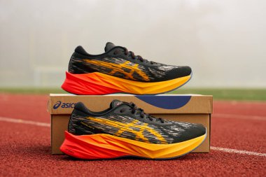 Modern Asics Novablast running shoes with black and orange design near box. Pair of sport shoes on stadium track. Stylish sneakers for sport exercises. Wroclaw, Poland - November 6, 2024 clipart