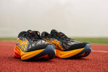 Kırmızı pist yüzeyinde spor yapmaya hazır renkli Asics Novablast koşu ayakkabıları giyen bir sporcunun ayaklarının yakın çekimi. Spor ayakkabılı sporcu bacakları, yaklaşın. Wroclaw, Polonya - 6 Kasım 2024