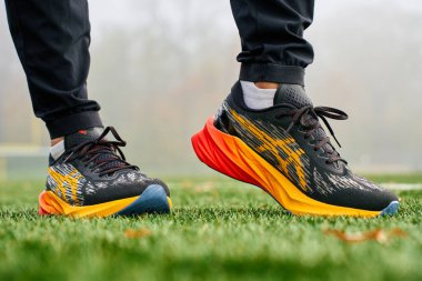 Yeşil çimenlikte renkli Asics Novablast giyen yakın plan atlet. Spor ayakkabılarıyla yeşil çimlerin üzerinde sporcu bacakları. Wroclaw, Polonya - 6 Kasım 2024