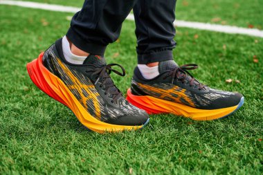 Yapay çimlerin üzerinde renkli Asics Novablast giyen yakın plan bir sporcu. Spor ayakkabılarıyla yeşil çimlerin üzerinde sporcu bacakları. Wroclaw, Polonya - 6 Kasım 2024