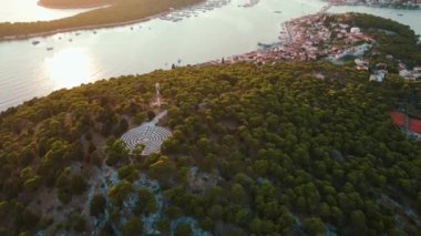 Gün batımında orman ağaçları ve dairesel labirentlerle kaplı adanın havadan görünüşü. Sahil kasabası olan deniz manzarası. Hırvatistan 'ın Rogoznica kentinde labirent