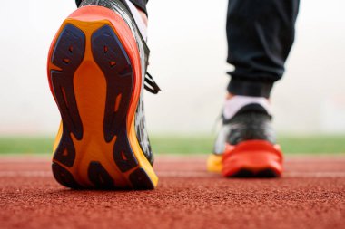 Kırmızı pist yüzeyinde spor yapmaya hazır renkli koşu ayakkabıları giyen bir sporcunun ayaklarının yakın çekimi. Spor ayakkabılı sporcu bacakları, yaklaşın. Fitness ve sağlıklı yaşam tarzı