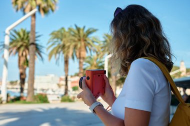 Sahil kasabasında günlük giysiler içinde fotoğraf çeken kadın bir gezgin. Tatil sırasında fotoğraf çekmek için turuncu retro fotoğraf makinesi kullanan bir kadın. Turist seyahat sırasında anıları yakalar