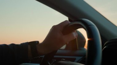 Direksiyon simidine yakın çekim yap. Adam gün batımında otoyolda araba sürüyor. Yolculuk konsepti