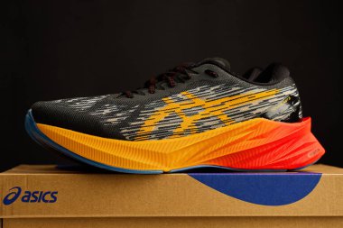 Modern Asics Novablast koşu ayakkabıları. Kutunun yanında siyah ve turuncu tasarım var. Arka planda bir çift spor ayakkabısı. Stüdyo çekimleri şık spor ayakkabılar. Wroclaw, Polonya - 6 Kasım 2024