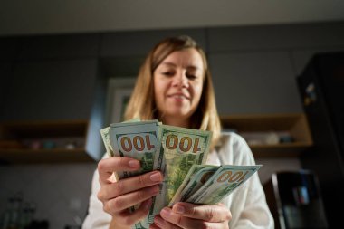 Evdeki banknotları sayan bir kadın. Amerikan dolarlarını elinde tutan kadın. Para yönetimi, zenginlik veya mali işlemler kavramı