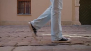 Yolda yürüyen kadın, yaklaşın. Spor ayakkabı giyen kadın bacaklarının kaldırım taşlı sokakta yürüdüğünü görmek. Ayakkabılı turist sokakta yürüyor.