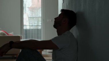 Karanlık odada yerde oturan depresif genç adam. Yalnızlık ve endişeyle kıvranan genç bir erkeğin silueti yüzünü ellerle kapatıyor. Akli dengesi bozuk biri.