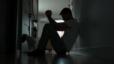 Karanlık odada yerde oturan depresif genç adam. Yalnızlık ve endişeyle kıvranan genç bir erkeğin silueti yüzünü ellerle kapatıyor. Akli dengesi bozuk biri.