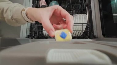 Bulaşık deterjanı tabletini içinde bulaşıklar olan açık bulaşık makinesine yakın çekim. Bulaşık makinesini temizleme döngüsüne hazırlıyorum. Modern ev aletleri