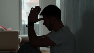 Karanlık odada yerde oturan depresif genç adam. Yalnızlık ve endişeyle kıvranan genç bir erkeğin silueti yüzünü ellerle kapatıyor. Akli dengesi bozuk biri.