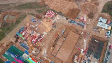 İnşaat alanının vinçlerle, vakıflarla ve inşaat malzemeleriyle hava görüntüsü. İkamet binası yapım aşamasında. Küçük kasabada yeni gelişmeler