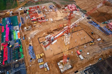 İnşaat alanının vinçlerle, vakıflarla ve inşaat malzemeleriyle hava görüntüsü. İkamet binası yapım aşamasında. Küçük kasabada yeni gelişmeler