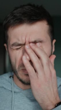 Yorgun adam gözlerini ovuşturuyor ve burnunun köprüsünü sıkıyor. Erkek yüzünün kapalı olması stres, yorgunluk ya da baş ağrısı yorgunluk, aşırı çalışma, akıl sağlığı ya da günlük mücadele belirtileri gösterir.