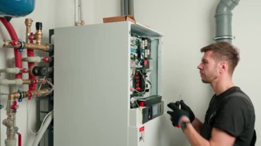 Isı pompasının iç kabloları üzerinde çalışan bir teknisyen, elektrik bağlantılarını inceliyor. Isıtma ve soğutma sisteminde uzman. Kontrol panelindeki vidaları sıkıştıran tornavidalı elektrikçi