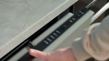 Bulaşık makinesinin açık kapılı kontrol panelinde elle başlatma düğmesine bas. Kadın modern ev aletleri kullanıyor, bulaşık makinesinde kirli bulaşıkları yıkamak için otomatik programı seçiyor.