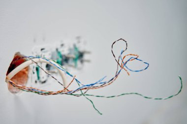 Duvar soketinden fırlayan açık bükülmüş ağ kablolarına yakın çekim. Veri kablosu kurulumunu veya onarımını gösteren tamamlanmamış kablo işi