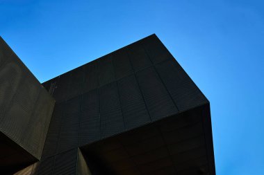 Açık mavi gökyüzüne karşı geometrik mimarisi olan modern siyah bir binanın alçak açılı görüntüsü. Minimalist estetiğe sahip çağdaş kentsel mimari tasarım