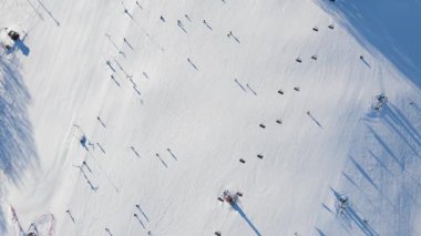 Kayakçılar ve asansörlü kayak pisti, karda kayak izleri ve ağaçların gölgeleri. Kış mevsiminde açık hava aktiviteleri için kayak merkezi
