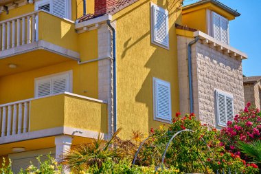 Beyaz panjurlu, balkonlu ve yemyeşil yemyeşil canlı bir villa. Hırvat köyünün geleneksel mimarisi. Sahil kasabasında yaz tatili için kiralık ev.