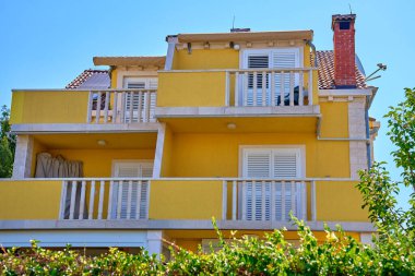 Beyaz panjurlu, balkonlu ve yemyeşil yemyeşil canlı bir villa. Hırvat köyünün geleneksel mimarisi. Sahil kasabasında yaz tatili için kiralık ev.