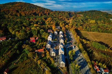 Canlı sonbahar ormanı yakınlarındaki modern yerleşim yerleri, hava manzarası. Küçük Avrupa kasabasındaki dağların yakınındaki yeşil alanları olan banliyö çevre dostu apartmanlar.