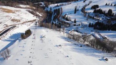 Güneşli bir günde kar yamaçları, sandalye kaldırışları, kiraz ağaçları ve orman ağaçlarıyla kaplı kış dağları manzaralı. Kayak merkezindeki kayakçılar ve snowboardcular. Kış sporları ve açık hava aktiviteleri