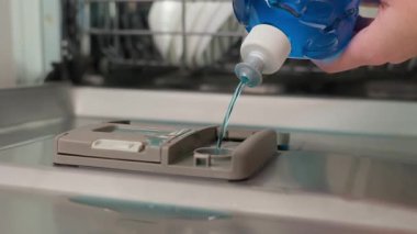 Bulaşık makinesinin deterjan bölmesine mavi bulaşık deterjanı döken kişiye yakın çekim. Mutfak aletlerinin işlemleri bulaşık yıkama bakımı