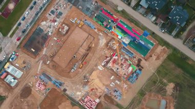 İnşaat alanının vinçlerle, vakıflarla ve inşaat malzemeleriyle hava görüntüsü. İkamet binası yapım aşamasında. Küçük kasabada yeni gelişmeler