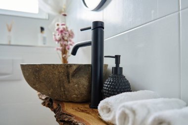 Modern banyo içinde taş havuz, siyah musluk, beyaz havlular ve kırsal ahşap tezgah var. Modern dairede doğal minimalist dekoru olan şık bir banyo.