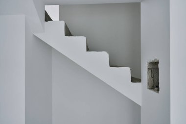 Modern minimalist iç mekanda tamamlanmamış beton merdiven. Ham inşaat elementleri ve beyaz duvarları olan yeni bir daire. Bina onarım altında