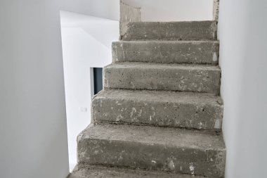 Modern minimalist iç mekanda tamamlanmamış beton merdiven. Ham inşaat elementleri ve beyaz duvarları olan yeni bir daire. Bina onarım altında