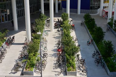 Danimarka 'nın Kopenhag kentindeki otoparkta park halindeki bisikletlerle dolu. Bitkiler ve modern mimari ile çevrili açık hava bisiklet park alanı. Çevre dostu ulaşım kavramı