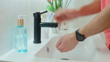 Banyo lavabosundaki akan suyun altında ellerini siyah muslukla yıkayan adamın yakın çekimi. Hijyen, temizlik ve kişisel bakım sabah rutin konsepti
