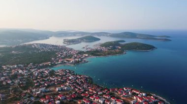 Kırmızı çatılı evleri, yemyeşil adaları ve turkuaz suları olan kıyı kasabasının havadan görünüşü. Adriyatik Denizi 'ndeki adalar. Hırvatistan 'daki Dalmaçya manzarasının panoramik görüntüsü